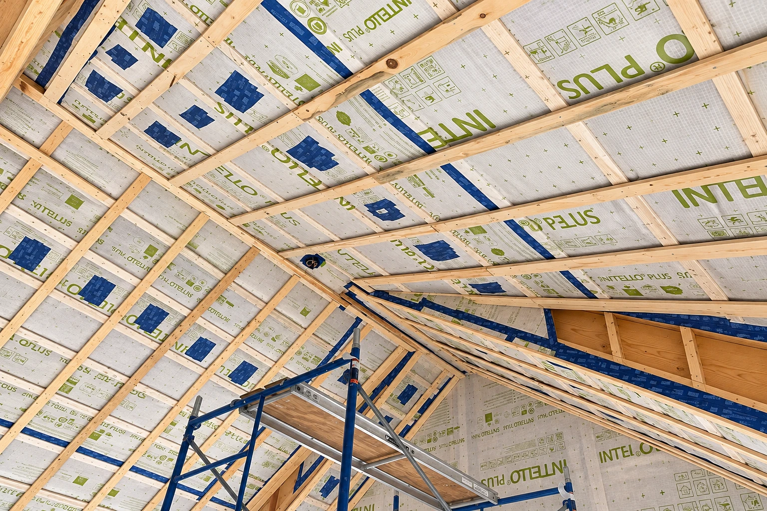 Wood roof trusses frame a ceiling lined with printed vapor barrier sheets, with a blue scaffold below.